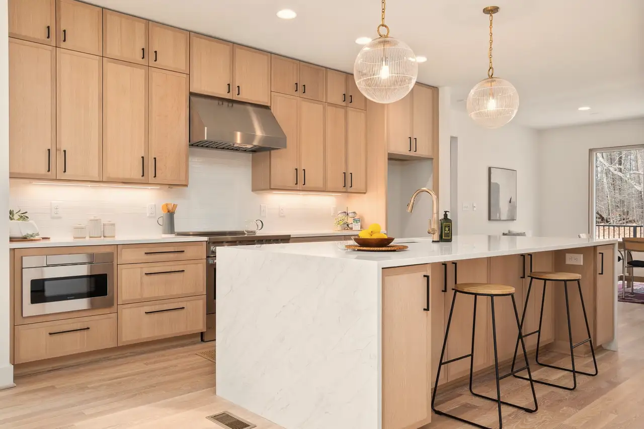 Bright kitchen with light oak cabinets, a marble island with stools and glass pendant lights