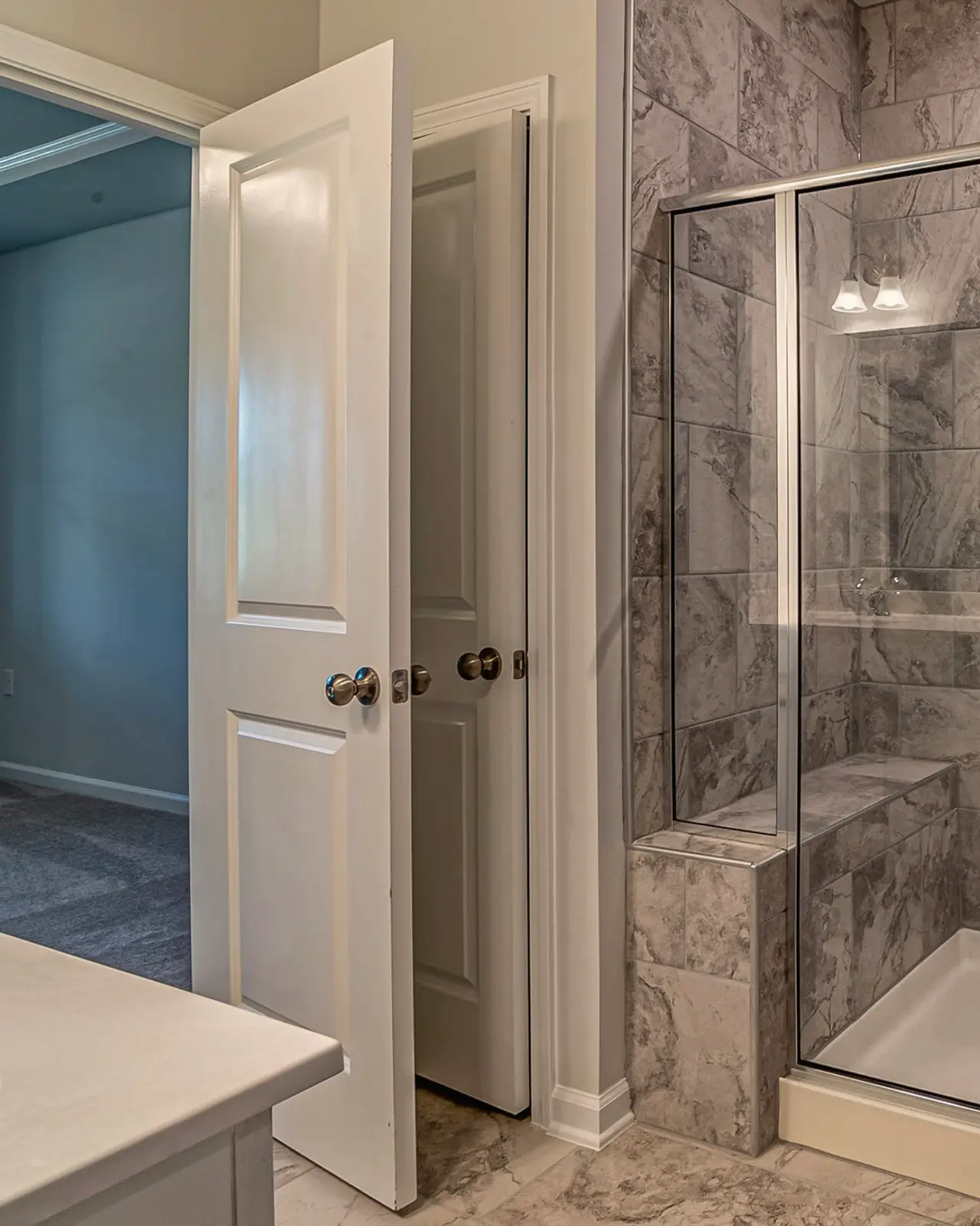 Marble-tiled walk-in shower with a glass door and built-in bench