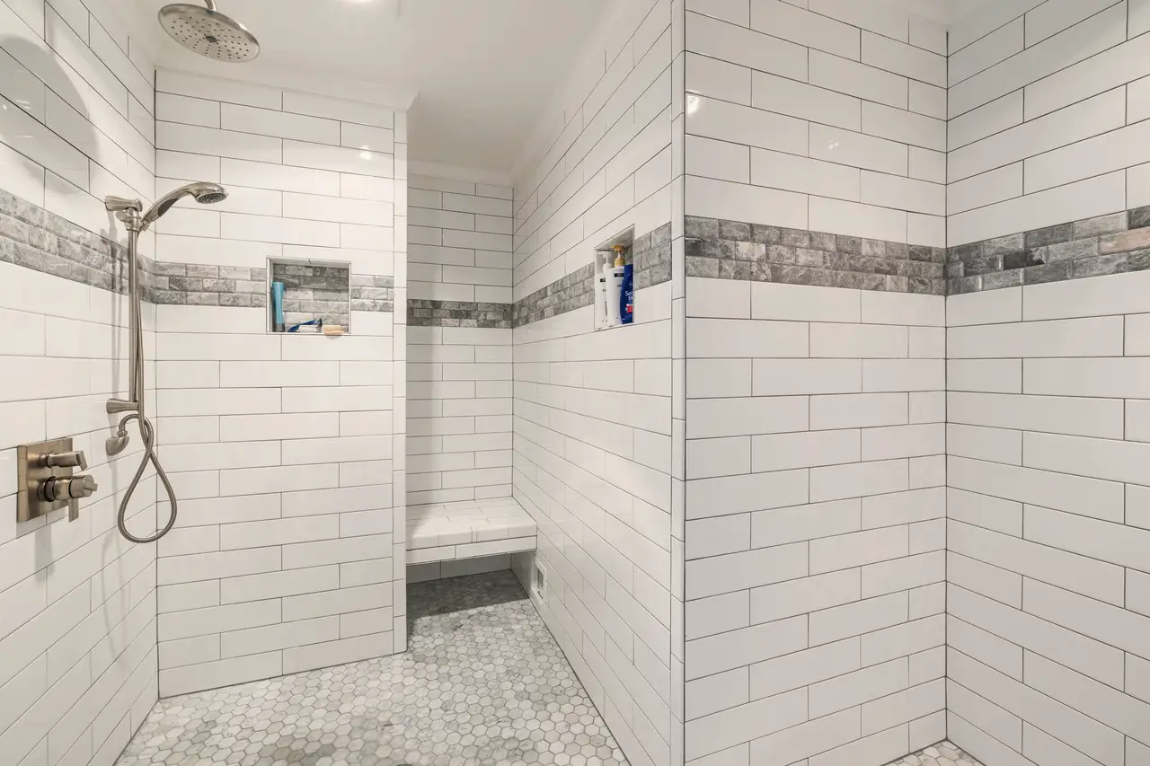 Walk-in shower finished in white subway tile with a grey border and mosaic floor